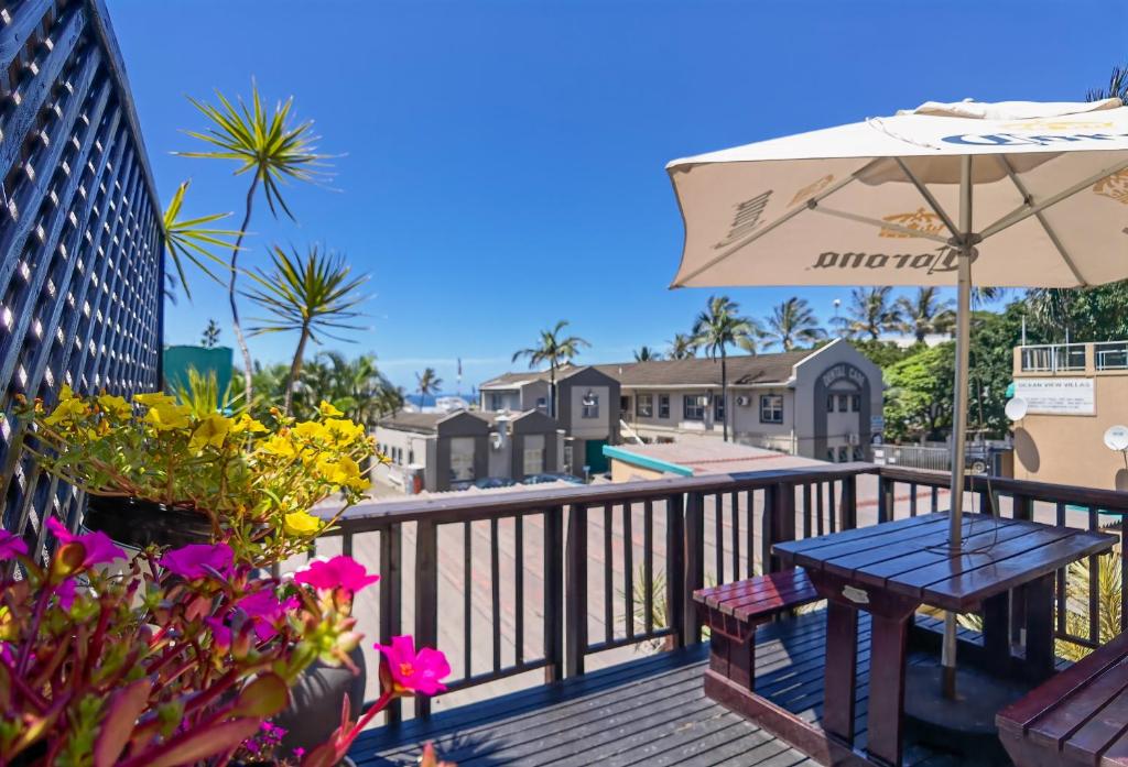 a deck with a table and an umbrella and flowers at Ocean View Villas in Ballito
