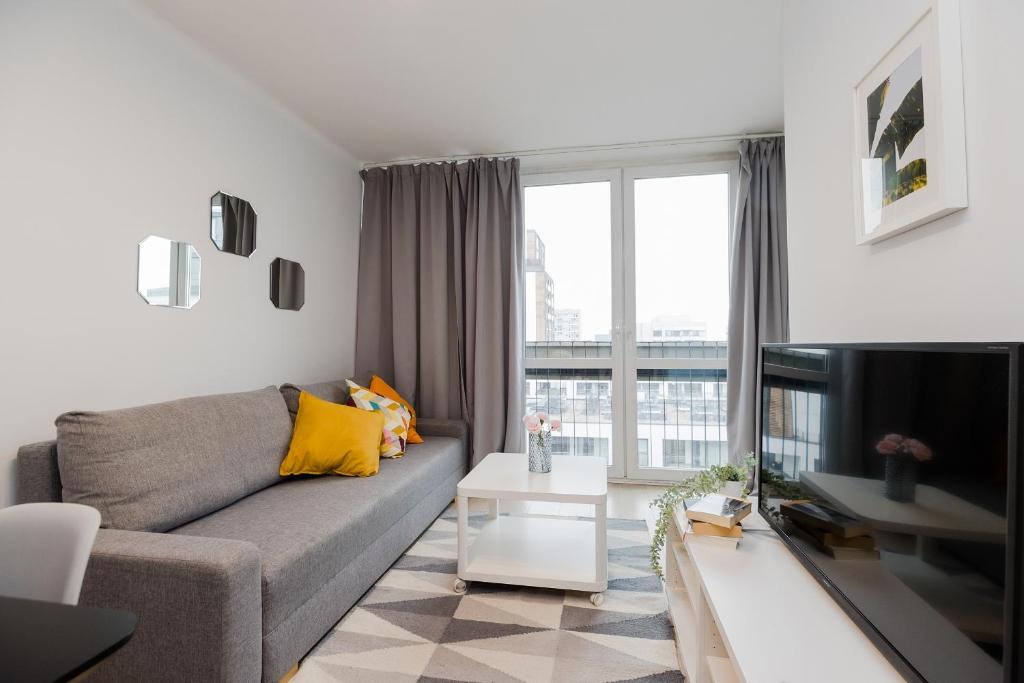 a living room with a gray couch and a large window at ShortStayPoland Grzybowska (B73) in Warsaw