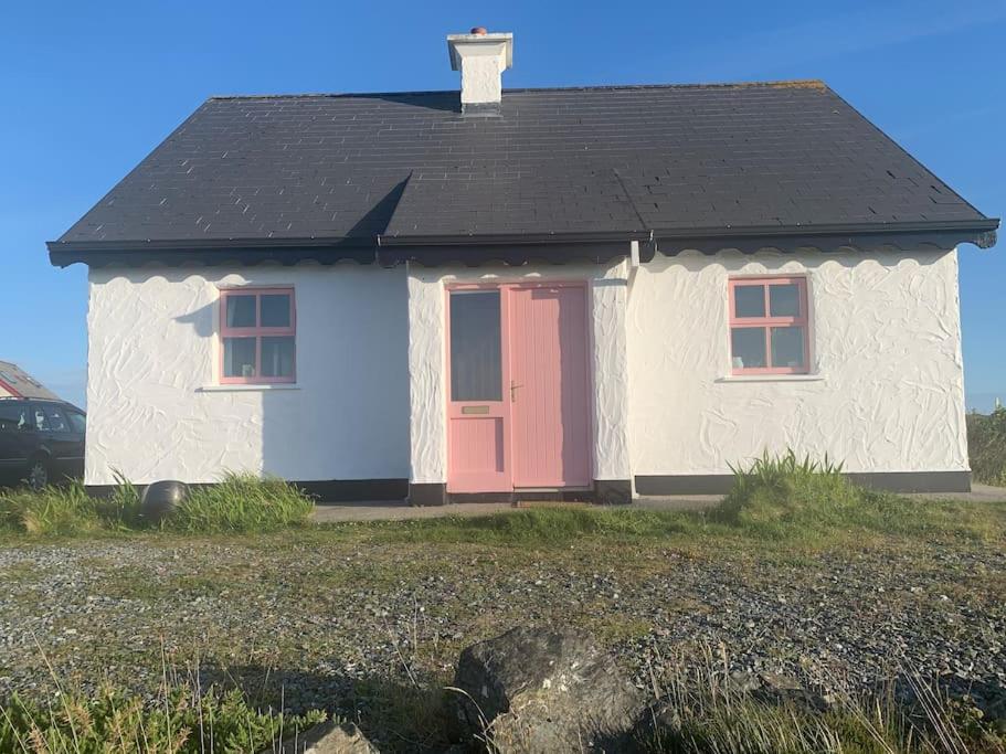 una pequeña casa blanca con una puerta roja en Pink Cottage, en Ballyconneely
