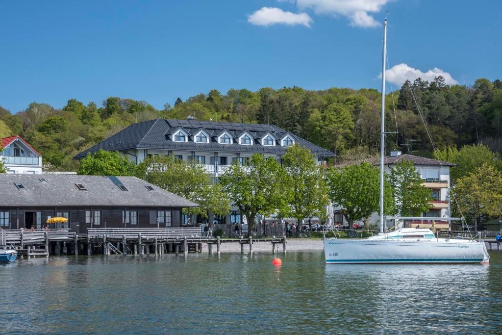 a boat sitting in the water next to a house at Ammersee-Hotel in Herrsching am Ammersee