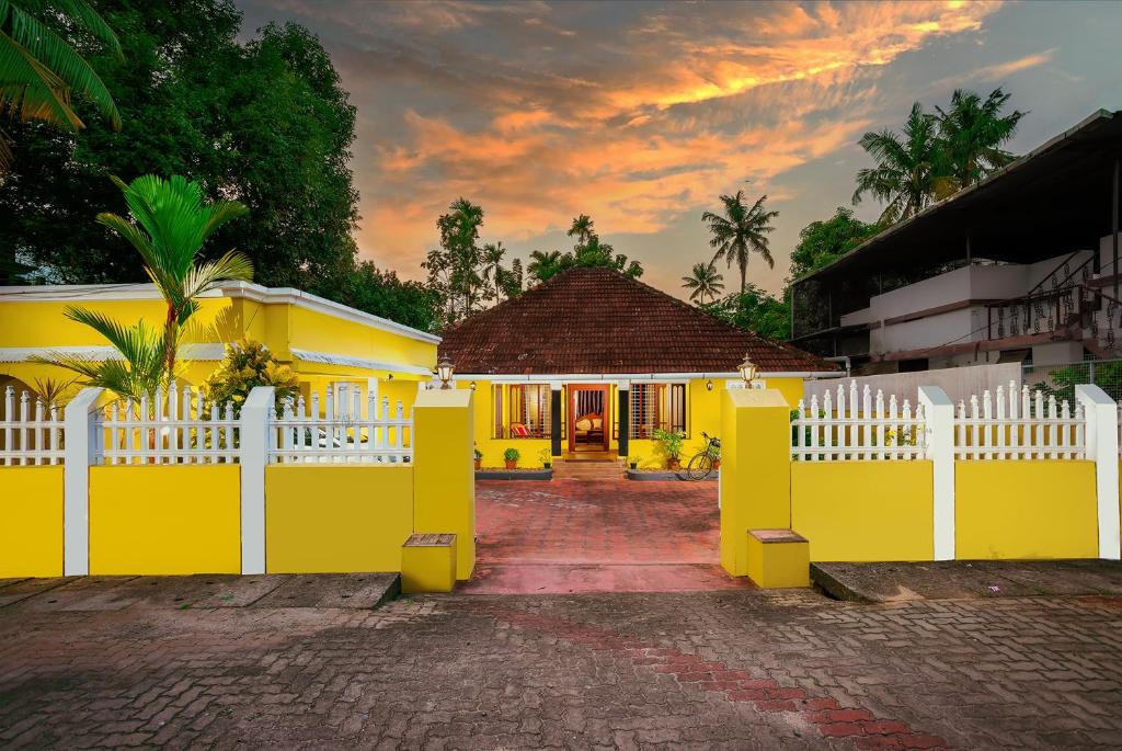 una casa amarilla con una cerca blanca delante de ella en The Mayflower - Heritage Villa en Alleppey