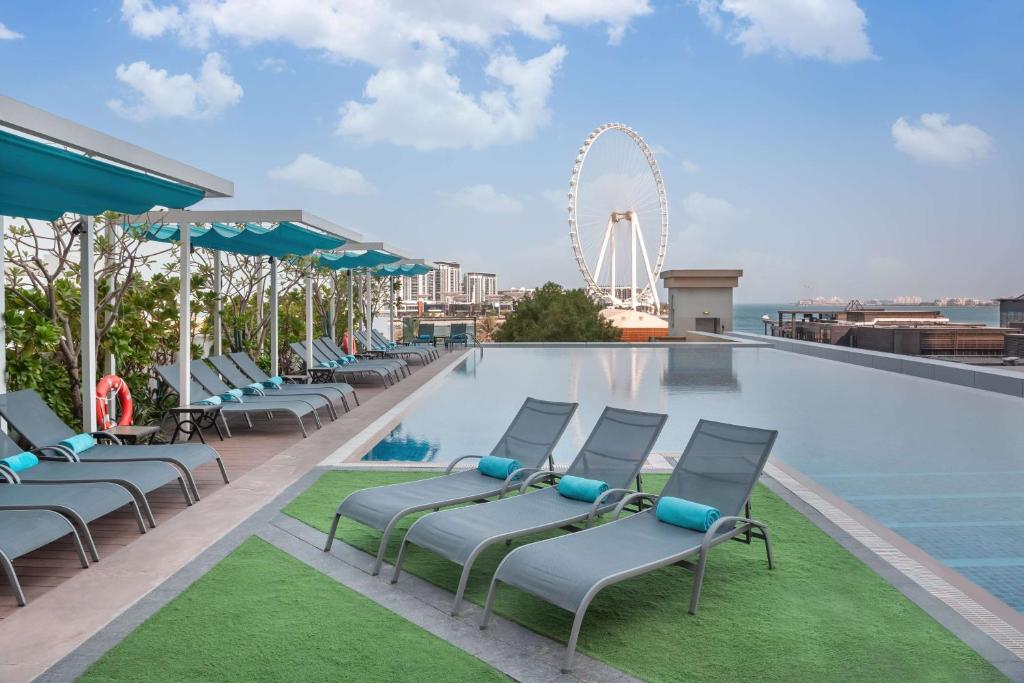 einem Pool mit Stühlen und einem Riesenrad im Hintergrund in der Unterkunft JA Ocean View Hotel in Dubai
