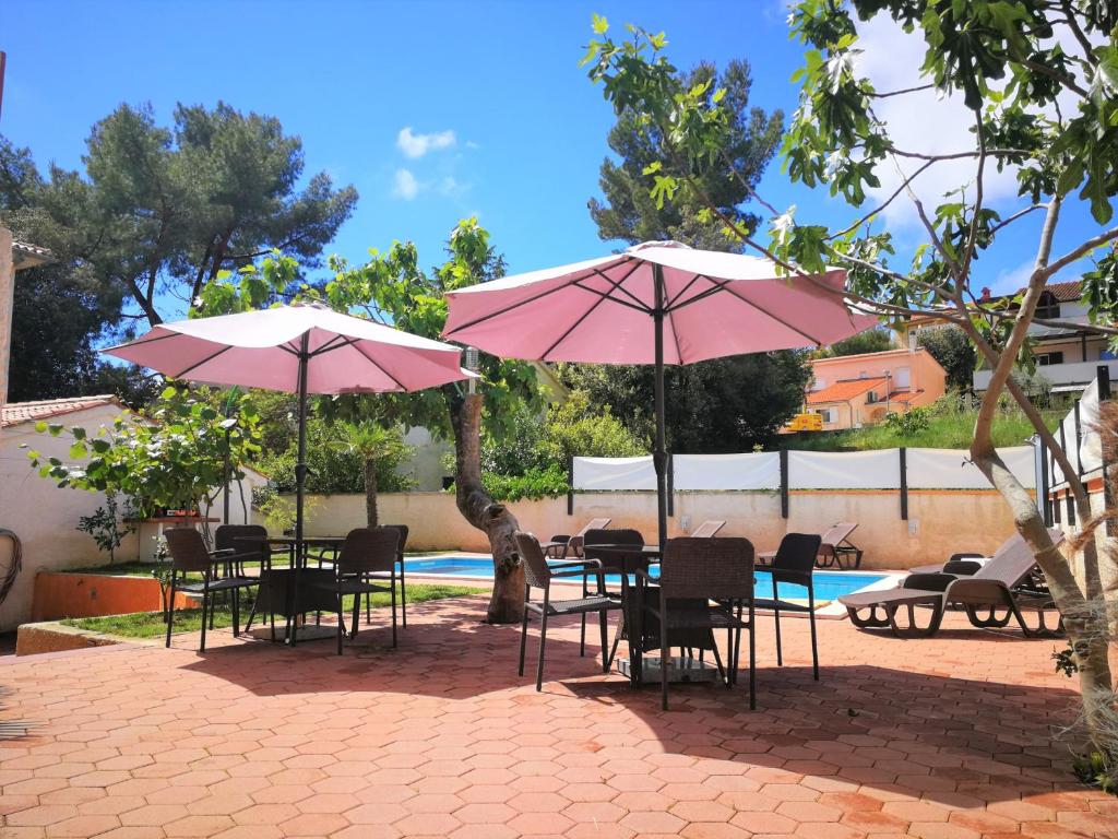 a group of tables and chairs with pink umbrellas at Apartments Bilic with garden & swimming pool - 50m from the beach in Pješčana Uvala 