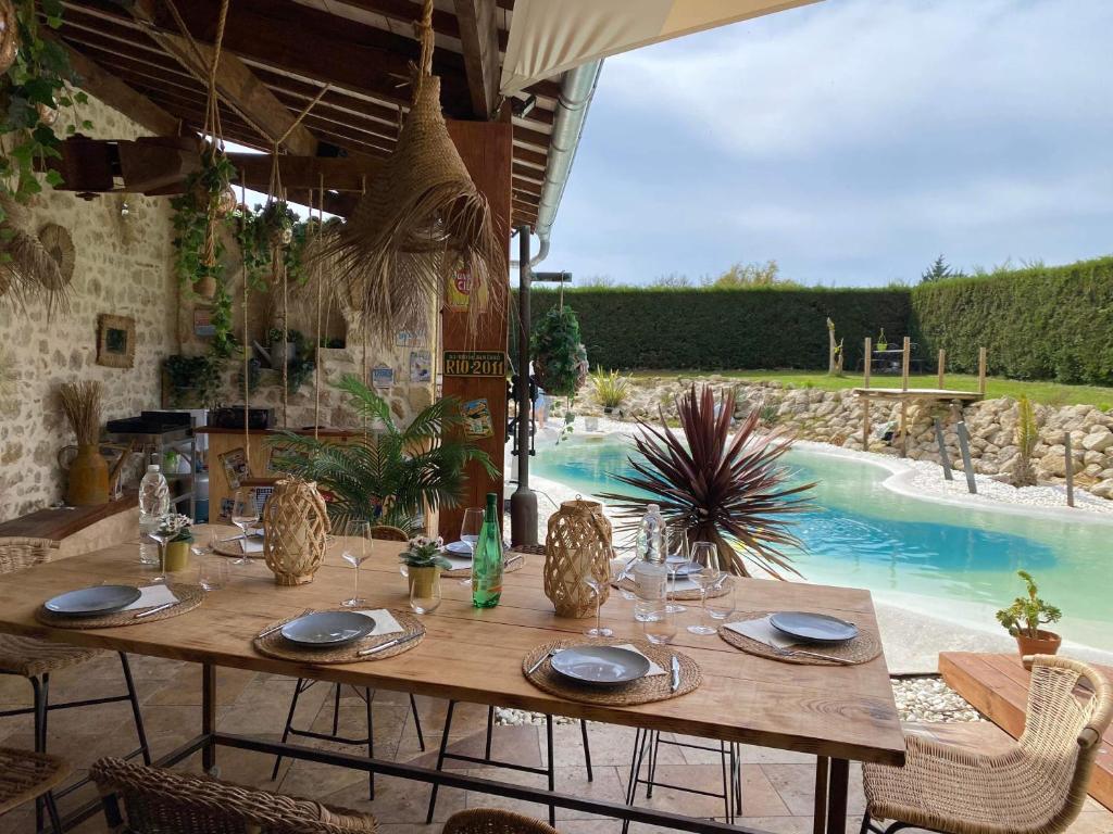 une table en bois dans un patio avec une piscine dans l'établissement Le Relais de la Chouette, à Berson