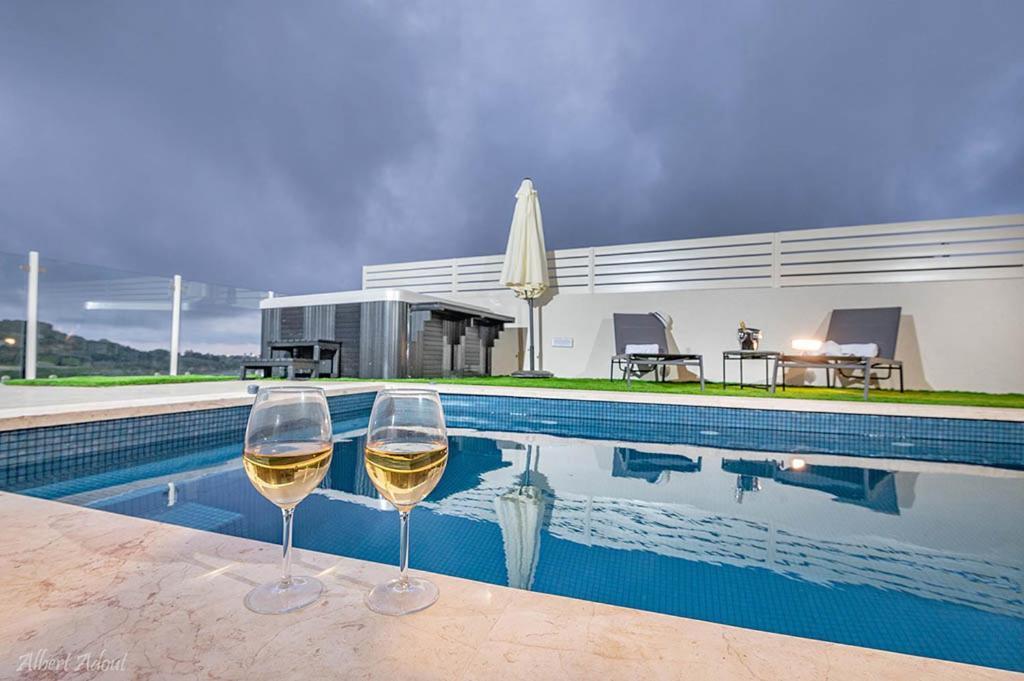 two glasses of white wine sitting next to a swimming pool at סוויטות Sol - סוויטות מהממות בגליל עם בריכה וג'קוזי במתחם in Gornot HaGalil