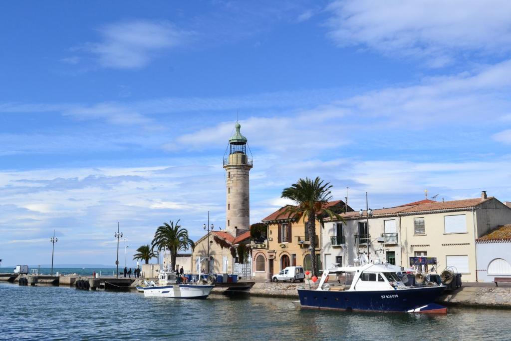 a lighthouse with two boats in a body of water at SOWELL RESIDENCES Les Sablons in Le Grau-du-Roi