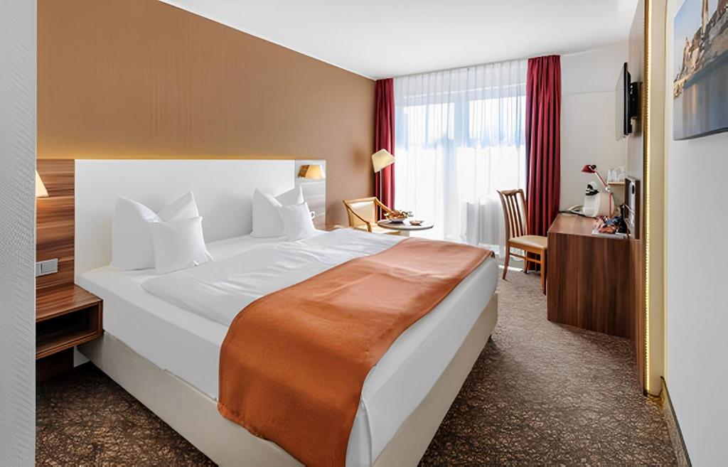 a hotel room with a large bed and a desk at PLAZA INN Regensburg in Regensburg