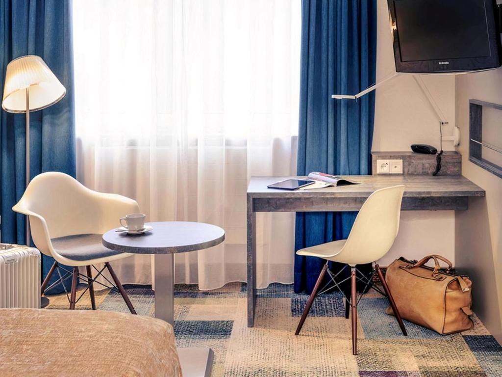 a room with a desk and two chairs and a table at PLAZA INN Regensburg in Regensburg