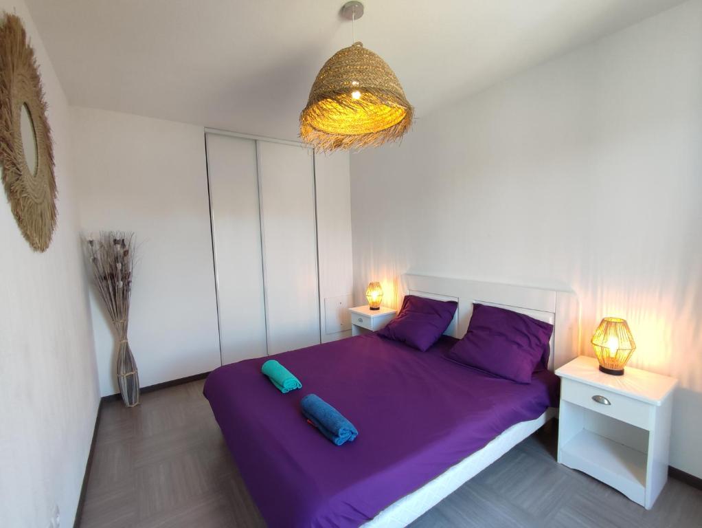 een slaapkamer met een paars bed met 2 tafels en een kroonluchter bij La terrasse de l'Imbut - Climatisation & Piscine in Gréoux-les-Bains