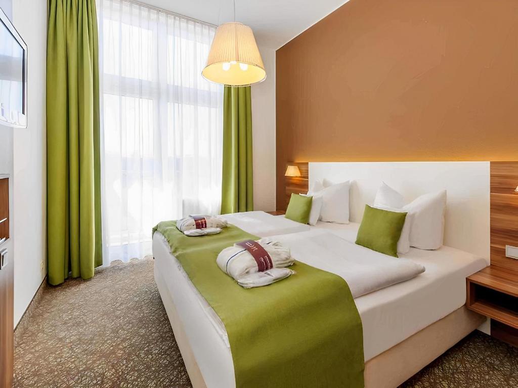 a bedroom with a large white bed with green accents at PLAZA INN Regensburg in Regensburg