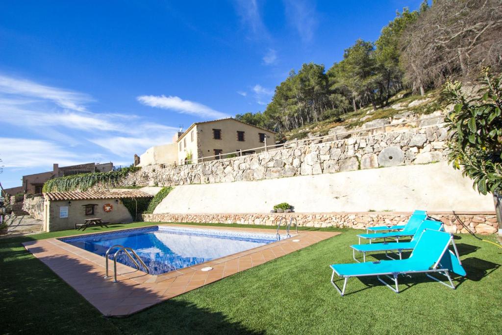 una piscina con 2 sillas azules y una pared de piedra en Catalunya Casas Sublime seclusion in Catalonia wine Region!, en Juncosa