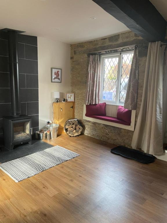 a living room with a fireplace and a window at Cotswold Coombe Cottage in Wotton under Edge