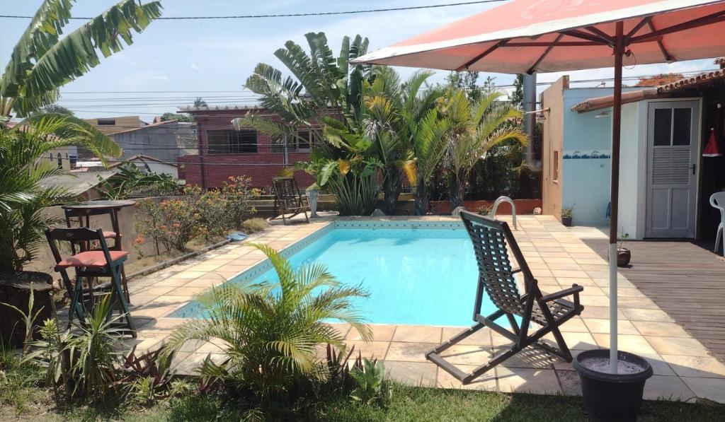 uma piscina com duas cadeiras e um guarda-sol em Guest House Flor de Laranjeira em São Pedro da Aldeia