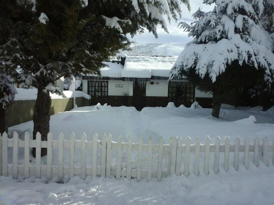 a white fence covered in snow in front of a house at Los Piros Alojamiento in Esquel