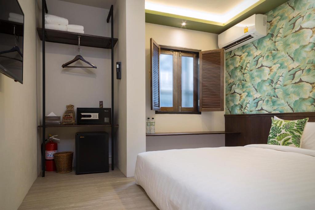 A compact guest room with a white bed, open storage, and a closed window.