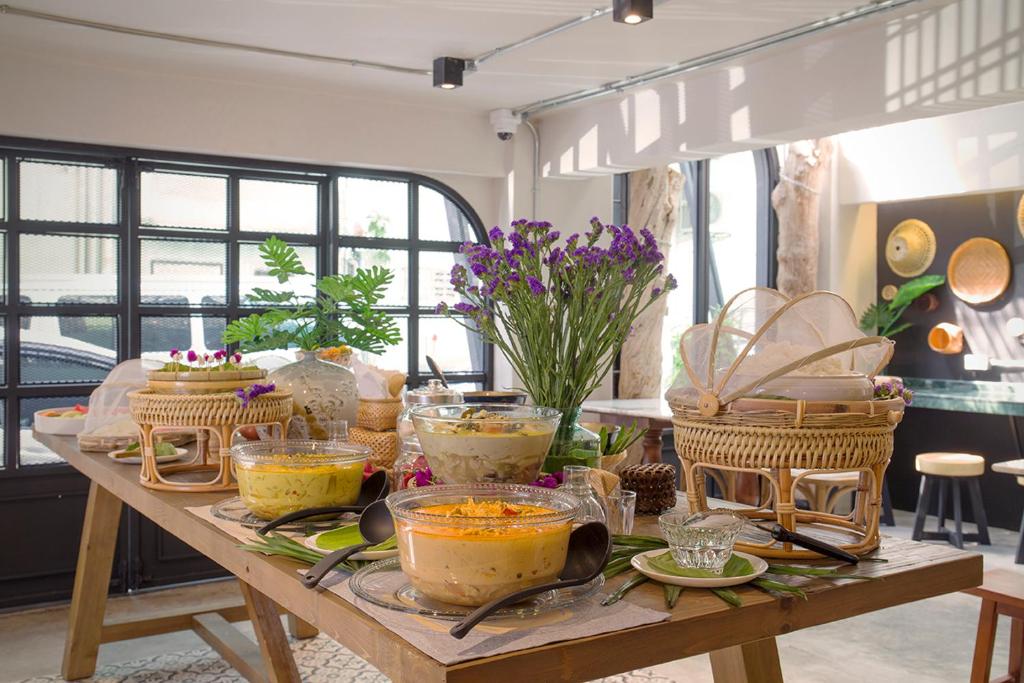 A decorated breakfast buffet table with bowls, baskets, fruit and flowers beside large windows.