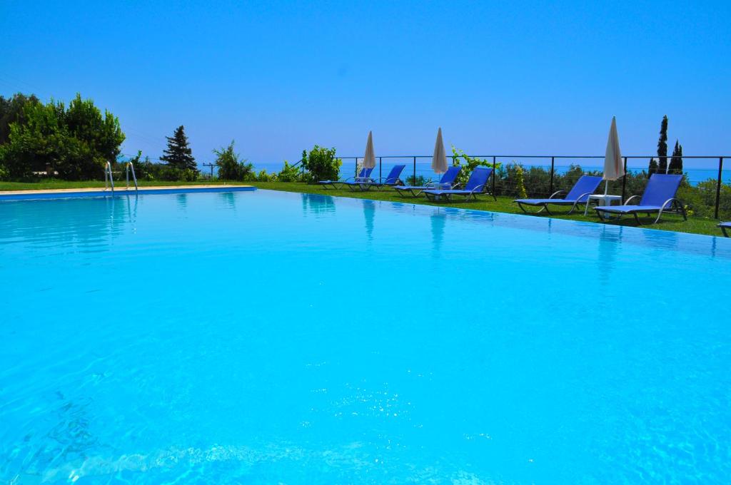 a large swimming pool with blue chairs and acean at Large apartment by the pool - Pelekas Beach, Corfu in Pelekas