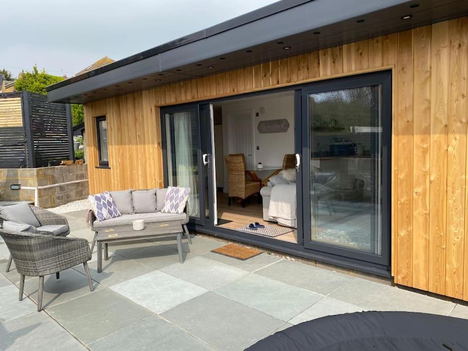 锡福德Spacious Studio Cabin with Sea/ Downs views Sole Use of HotTub in Seaford的天井设有滑动玻璃门、沙发和椅子