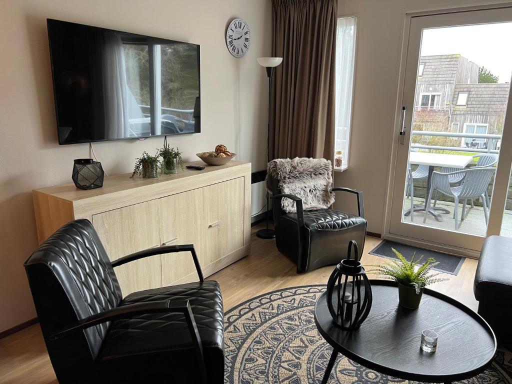 ein Wohnzimmer mit einem TV, einem Tisch und Stühlen in der Unterkunft Appartement Ut & Thus, Resort Amelander Kaap in Hollum