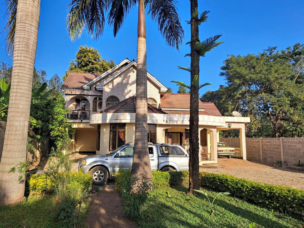une voiture garée devant une maison avec des palmiers dans l'établissement Villa Jane, à Arusha