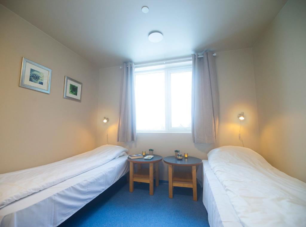two beds in a room with a window and two tables at Sjøholt Sommerhotell in Ørskog