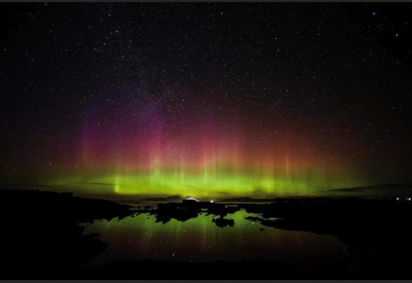 an aurora in the sky with a reflection in the water at Borve House, Kilchoan in Kilchoan