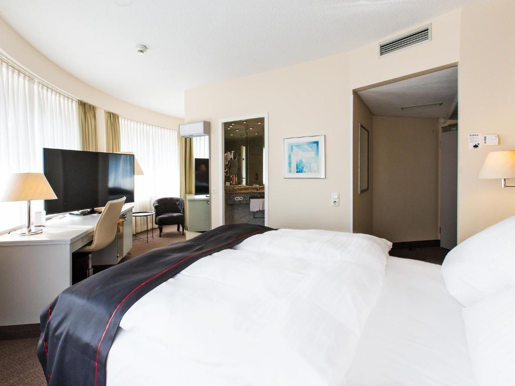 a hotel room with a large white bed and a desk at DORMERO Hotel Dessau-Roßlau in Dessau