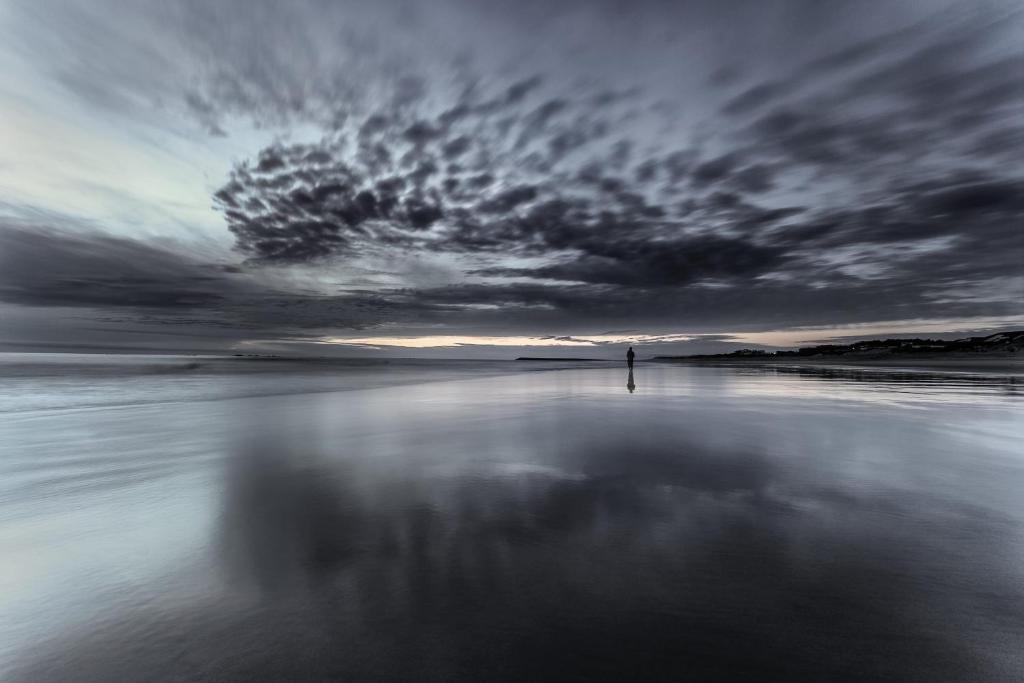 eine Person, die am Strand unter einem wolkigen Himmel steht in der Unterkunft Apartamento na Vila in Fão