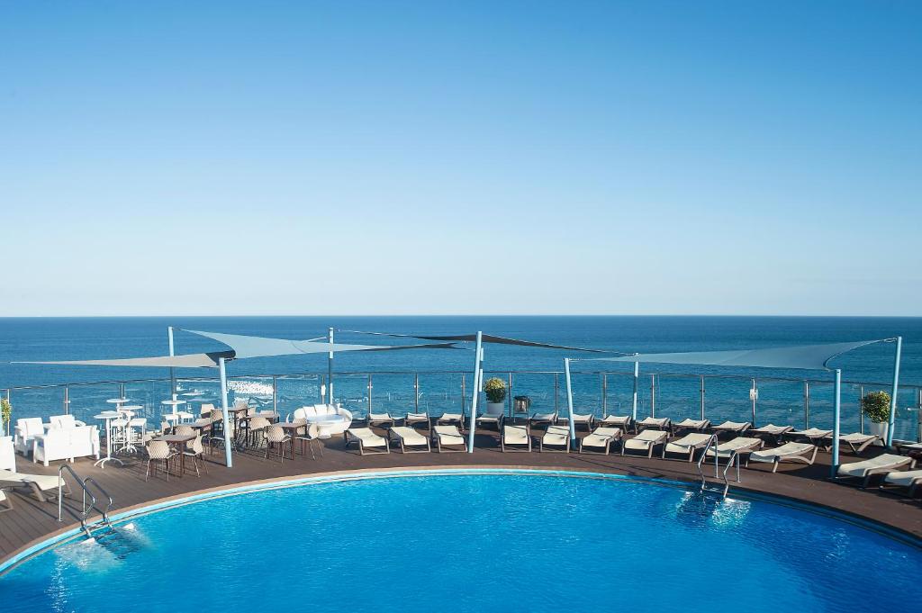 una piscina con sedie e l'oceano sullo sfondo di Hotel El Puerto by Pierre Vacances a Fuengirola