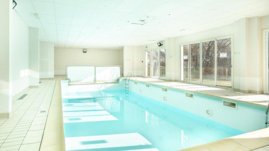 a large swimming pool with blue water in a room at Appart. lumineux à St-Sorlin d'Arves (Sybelles) in Saint-Sorlin-dʼArves