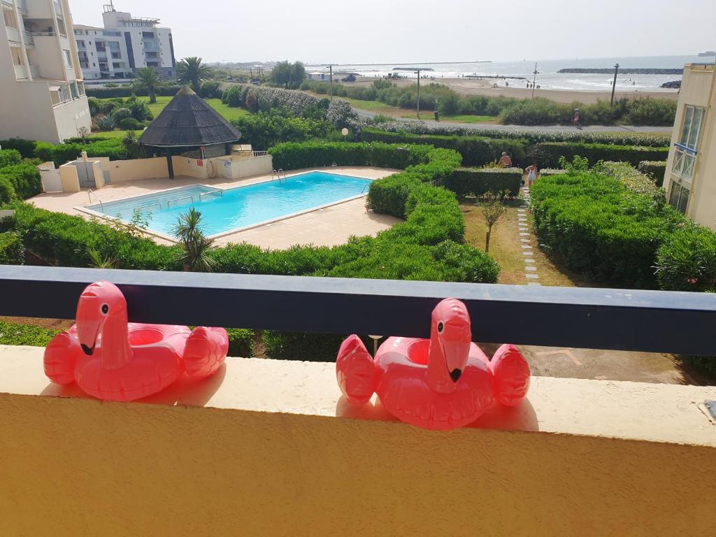 two rubber flamingos sitting on a balcony with a pool at SAVANNA BEACH I Joli T2 piscine vue mer Cap d'Agde in Cap d'Agde