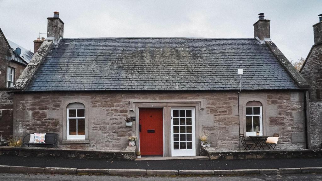 uma antiga casa de pedra com uma porta vermelha em Woodview Cottage em Glamis
