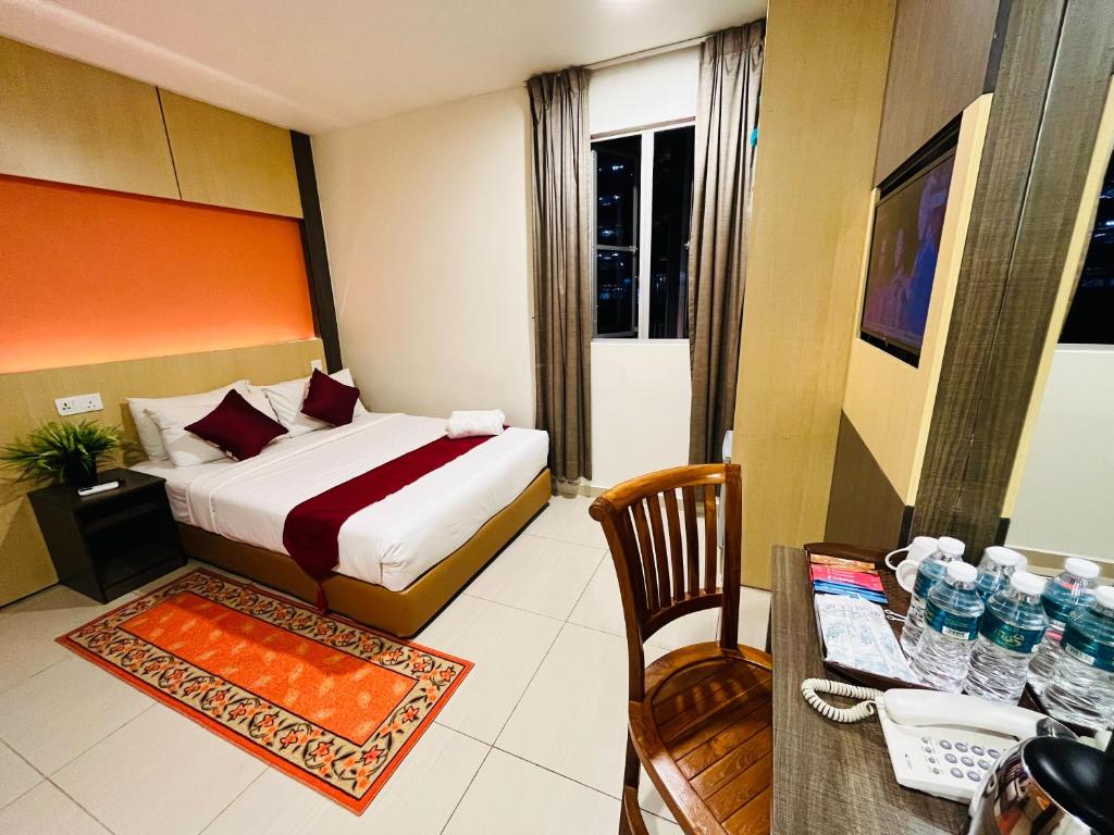 A compact guest room has a double bed, narrow desk, chair, television, and a curtained window.