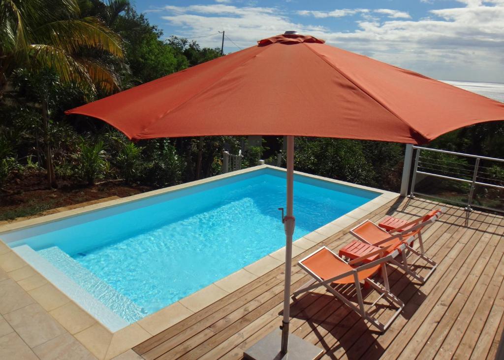 ein Sonnenschirm und Stühle neben einem Pool in der Unterkunft TOUDOU DOUDOU in Deshaies