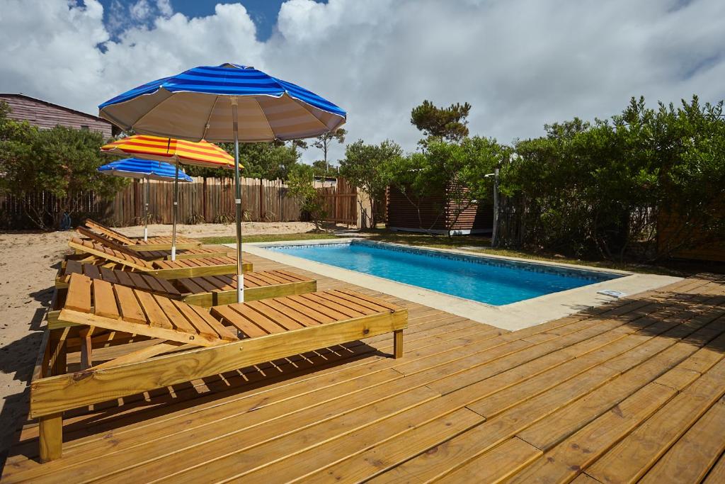 a wooden deck with an umbrella and benches next to a swimming pool at Aves del Paraiso 1 in Punta Del Diablo