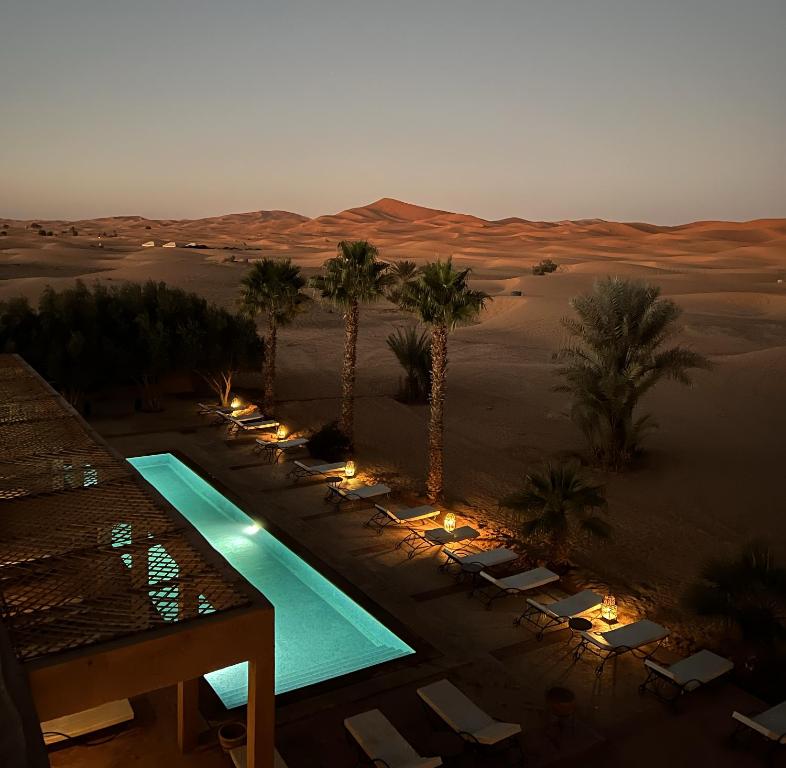 a resort in the desert with a swimming pool and palm trees at Kanz Erremal in Merzouga