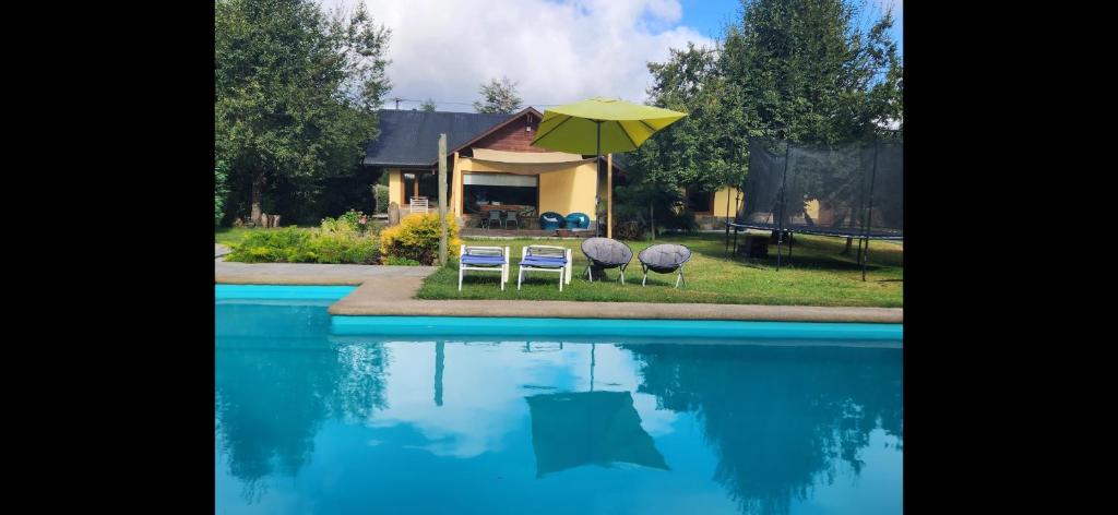 duas cadeiras e um guarda-sol junto a uma piscina em Casa Campestre con piscina compartida em Villarrica