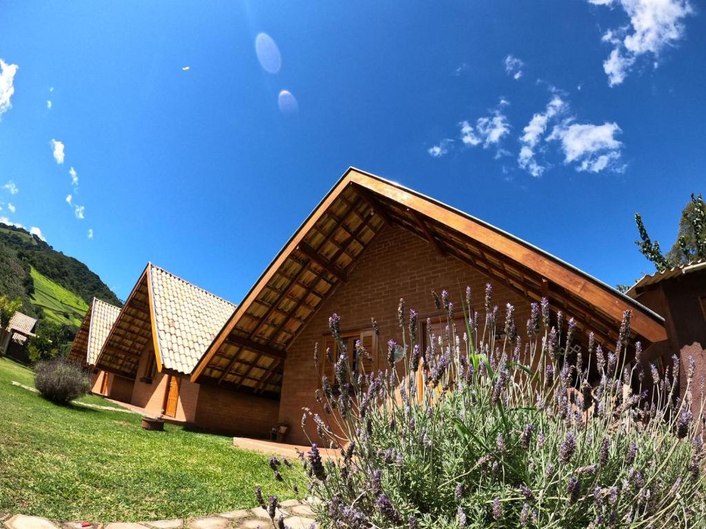 une maison avec un toit en pente et un champ d'herbe dans l'établissement Chalés Maranata, à São Bento do Sapucaí