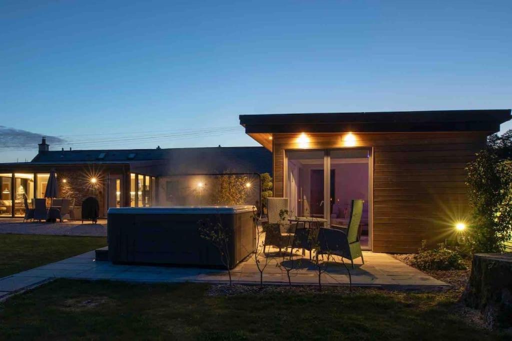 ein kleines Haus mit einer Terrasse in der Nacht in der Unterkunft Amazing Cottage & detached Annex sleeps 8, Extra Deep Hot tub, Super Fast wifi, New for 2024 is the addition of Wood Fired Sauna in Castle Douglas
