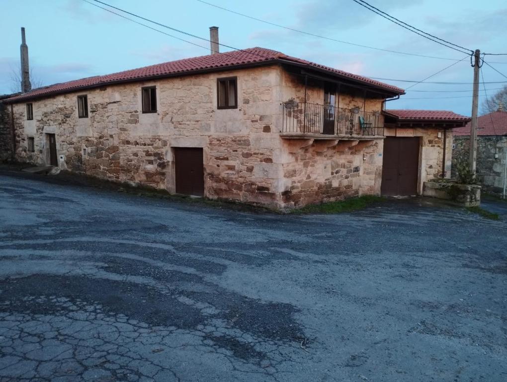 una vieja casa de piedra con un estacionamiento delante de ella en Casa Xulián, en Monterroso