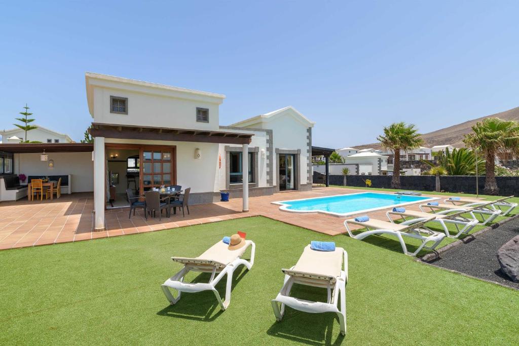 een huis met een gazon met ligstoelen en een zwembad bij Villa Esterlicia in Playa Blanca