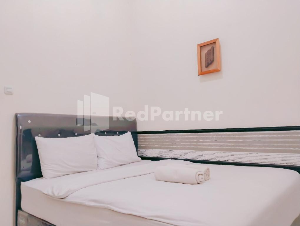 a bed with white sheets and a towel on it at Siliwangi Guest House Syariah Tasikmalaya Mitra RedDoorz in Tasikmalaya