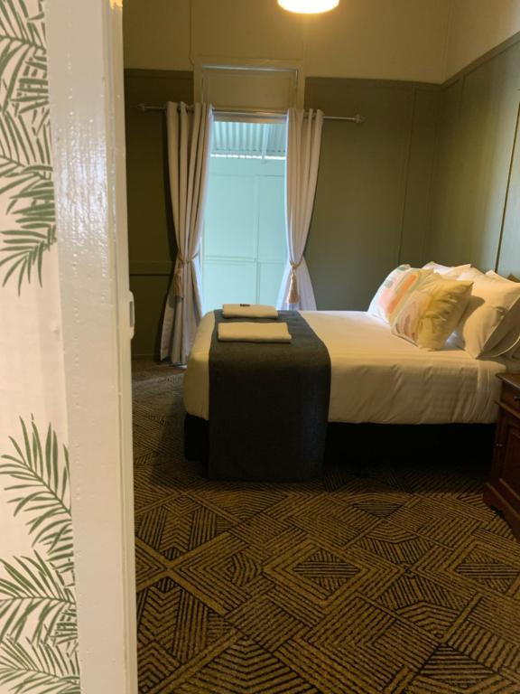 a bedroom with a bed with a ottoman in front of a window at Tyalgum Hotel in Tyalgum