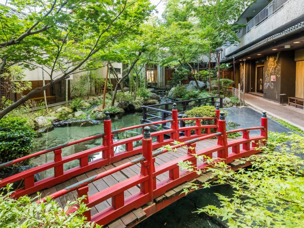 un pont rouge sur une rivière dans un jardin dans l'établissement Japanese Onsen Ryokan Kohakuen, à Fuefuki