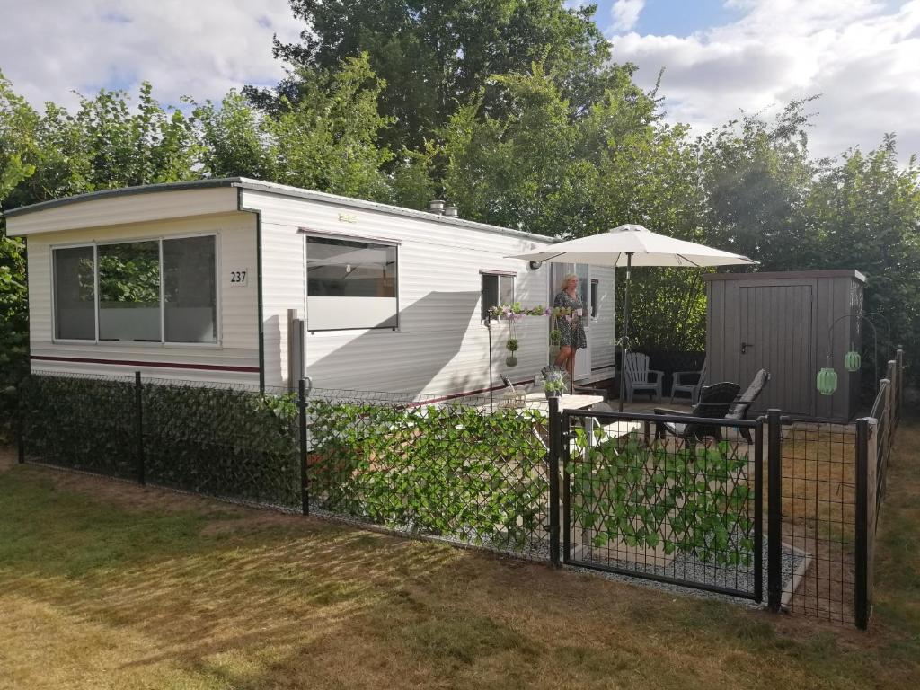 a tiny caravan with a fence and an umbrella at Stacaravan op 5 Sterren Vakantiepark De Kuilart Friesland aan het Meer met Zwembad 5P 237 in Koudum