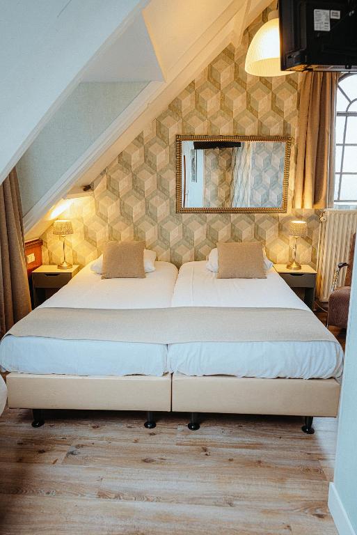 a bedroom with two beds and a mirror on the wall at Hotel Johannes Vermeer Delft in Delft