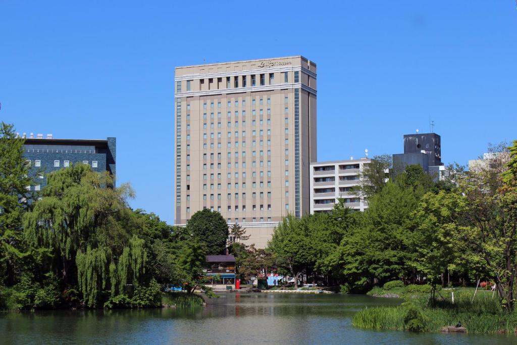 Hotel Lifort Sapporo في سابورو: مبنى كبير امام نهر به اشجار
