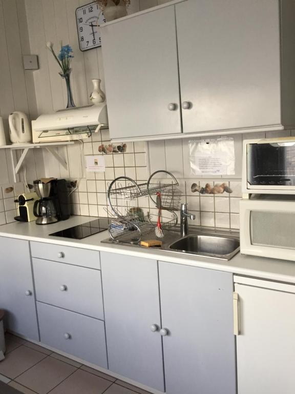 cocina con armarios blancos, fregadero y microondas en Petite maison dans le jardin en Ars-en-Ré