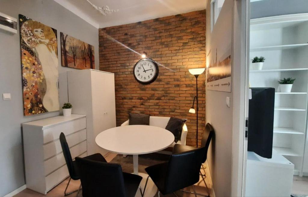 Cette chambre dispose d'une table, de chaises et d'une horloge sur un mur en briques. dans l'établissement Urban Nest Apartments Szewska 21-5, à Cracovie