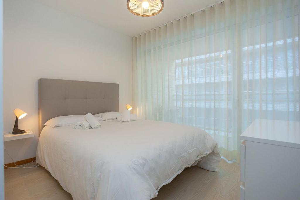 a white bedroom with a white bed and a window at Galante Beach Apartment II in Figueira da Foz